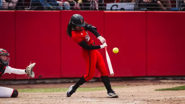 Desirae Spearman swinging the bat and connecting on a pitch while wearing an all red jersey for softball