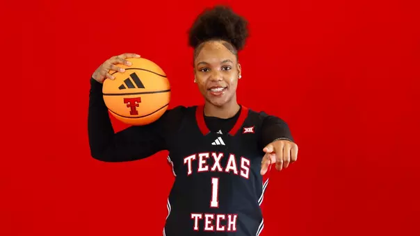 Destinee Hooks pointing to the camera with a basketball on her shoulder.