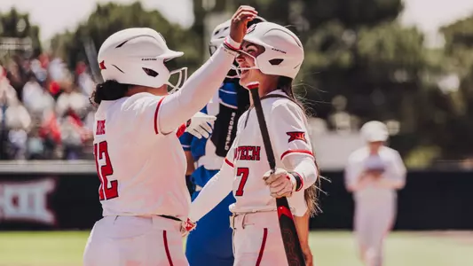 Logan Halleman and Jasmyn Burns hug to celebrate a run being score while wearing white Softball jerseys