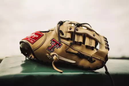A tan Texas Tech embroidered glove on sits on the dugout fence