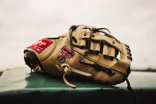 A tan Texas Tech embroidered glove on sits on the dugout fence