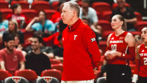 Tony Graystone coaching on the sidelines of a volleyball match with his hands behind his back