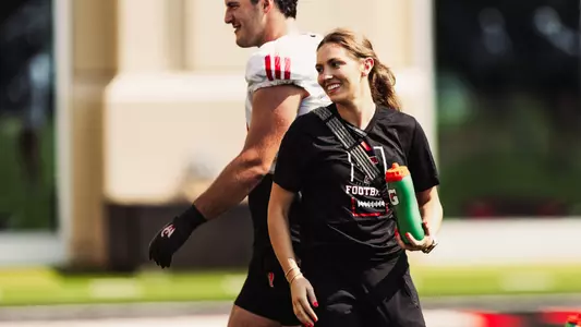 Lexye Price hold a Gatorade bottle in front of a football player at practice