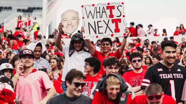 Two Texas Tech fans hold up a sign that says "What's Next" with a picture of Joey McGuire in the stands of Galaxy Stadium.