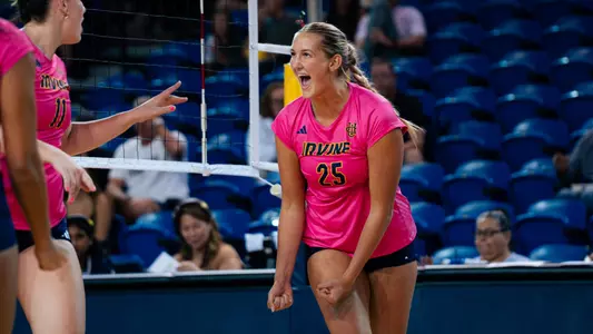 Ava Gronemeyer wearing a pink UC Irvine jersey celebrates with her teammate on the court during an NCAA women's volleyball match.