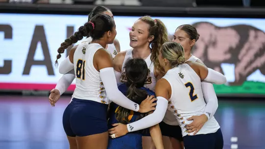 Jessica Bates smiles as she's surrounded by her teammates in a celebration on the volleyball court.