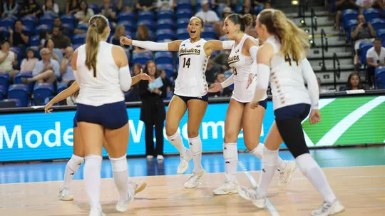 Brianna Brewer celebrates with her teammates after winning a point in an NCAA women's volleyball match.