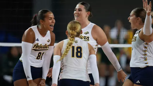 UCI women's volleyball players Memphis Burnett, Taylor Boice, and Nicole Feliciano celebrate on the court after winning a point.