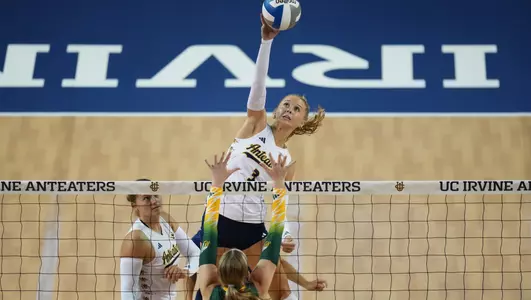 Photo of Abby Pekrul making contact with the ball above the net on a middle attack.