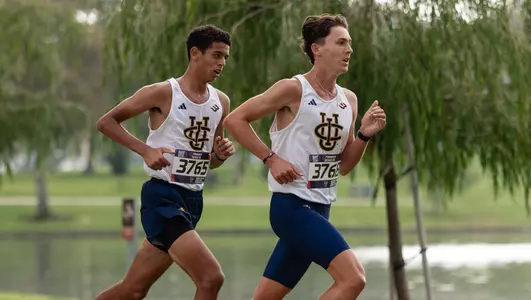 Ziyad Abdallah follows behind Jimmy Markowicz in front of trees and a lake during a cross country race at Mason Regional Park.