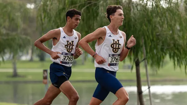 Ziyad Abdallah follows behind Jimmy Markowicz in front of trees and a lake during a cross country race at Mason Regional Park.