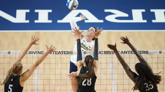 Taylor Boice hits the ball over three blockers in an NCAA women's volleyball match.