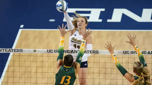 Jessica Bates hits the ball over a double block in an NCAA women's volleyball match.