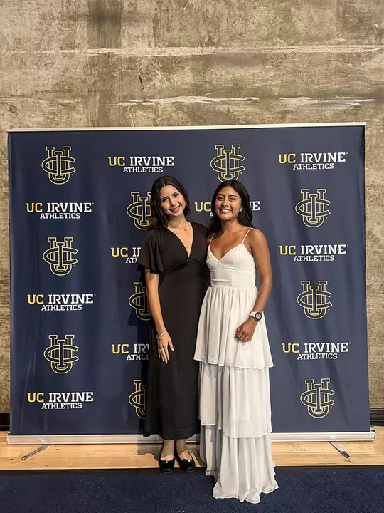 Marjourie Lopez and Cynthia Herrera pose for a photo in front of a UC Irvine Athletics backdrop at an awards event.