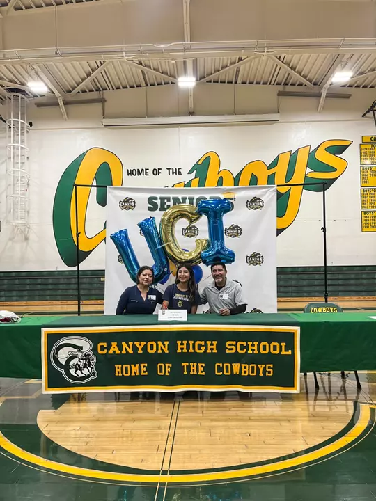 Cynthia Herrera sitting in the middle of her mother and father at an event at Canyon High School announcing her signing with UC Irvine cross country/track & field.