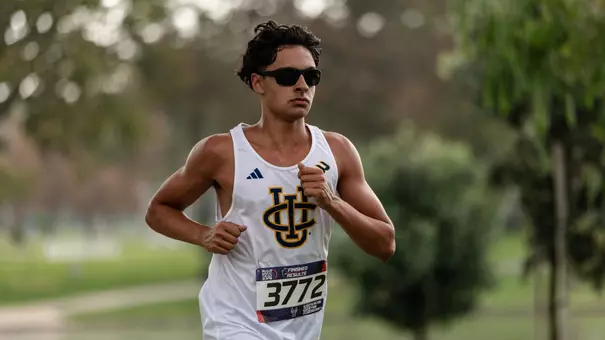 Javin Schmitt wearing a white UCI uniform running a cross country course at the park.
