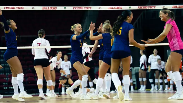 UC Irvine women's volleyball players high five and celebrate on the court after winning a point.