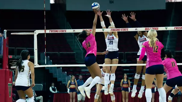 Brianna Brewer wearing a pink jersey and blue shorts tips the ball over the block in an NCAA women's volleyball match.