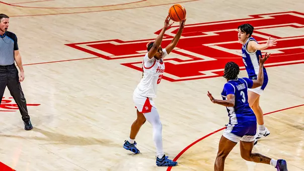 Kayla King with arms in the air and basketball in hand against two Kansas State defenders