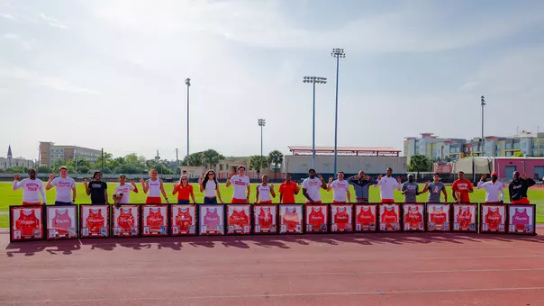 19 men and women standing side by side with their framed jerseys and holding the Cougar paw sign
