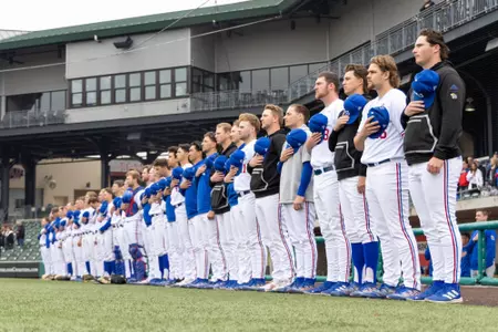 A row of baseball players stand with their hats in their hands for the national anthem