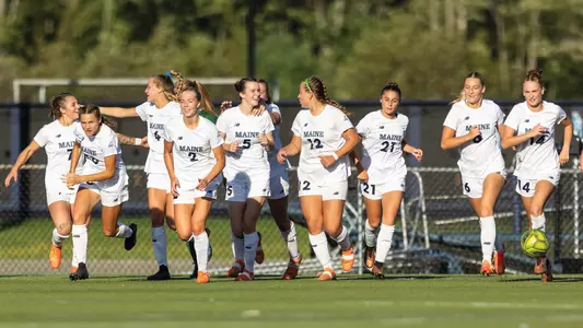 Women's soccer runs up the field together after a goal.