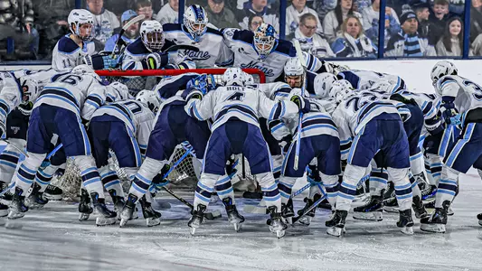 Maine men's hockey huddles around the net.