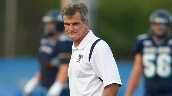 Football coach Jack Cosgrove walking on the field with a white shirt.