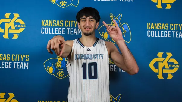 Atuka Bakhtadze shows a "Roo Up" hand sign and points at the camera in front of a KC Roos backdrop