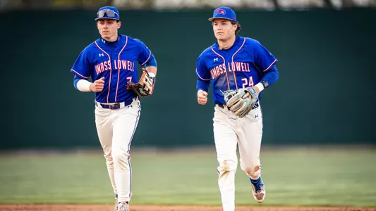 Two UMass Lowell baseball players running off the field and getting ready for their at-bats after the inning ended