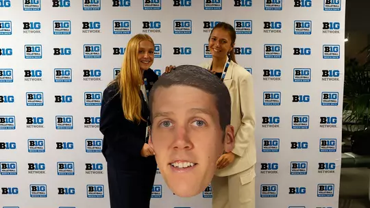 Sydney Dowler and Sam Csire holding a giant cardboard cutout of head coach Adam Hughes' head at 2023 Big Ten Volleyball Media Day