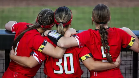 Bailey Murphy, Caitlyn Cornwell, and Genevieve Ebaugh embrace in the dugout during the game.