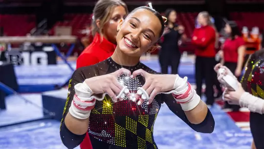 Gianna Ruffing making a heart shape with her hands during a Maryland gymnastics meet