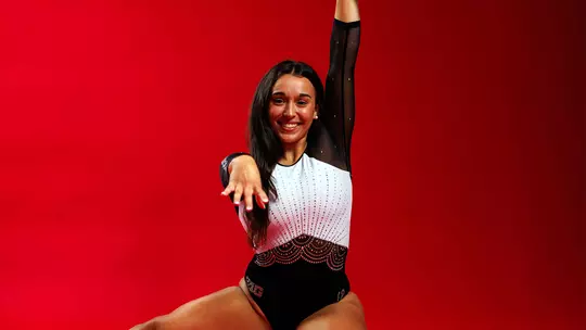 Studio photo of Aine Reade in a gymnastics pose in front of a red backdrop