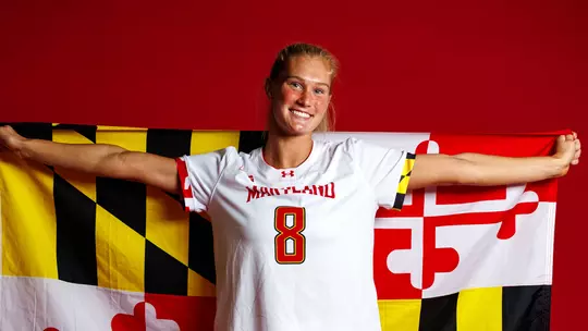 Studio photo of Lauren LaPoint holding a Maryland flag across her back in front of a red backdrop