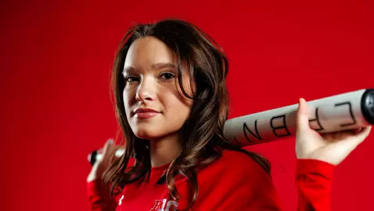 Studio photo of Jaylee Williams holding a bat across her shoulders in front of a red backdrop