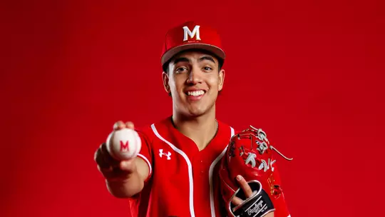 Studio photo of David Mendez holding a baseball in front of a red background