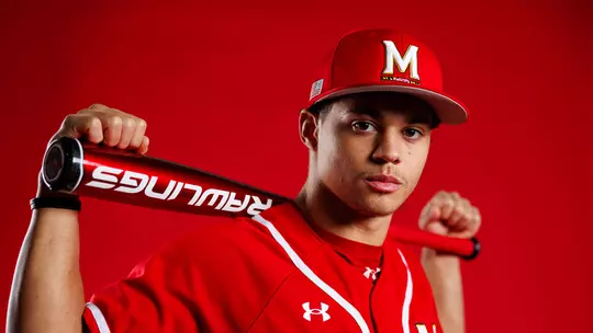 Studio photo of Bud Coombs with a bat across his shoulders on a red background