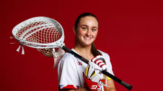 Studio photo of JJ Suriano holding a goalie stick on a red background