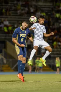 UNF men's soccer player and opponent compete for header in the air