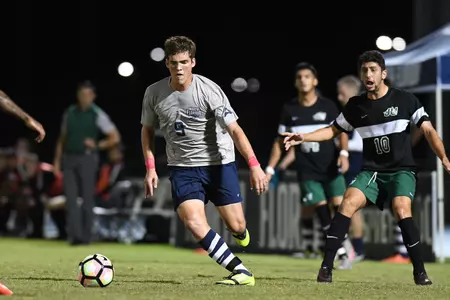 UNF men's soccer player dribbles up the field