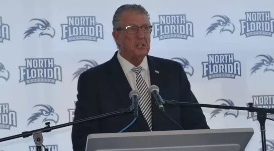Lee Moon stands behind the podium speaking to a crowd at UNF athletic event