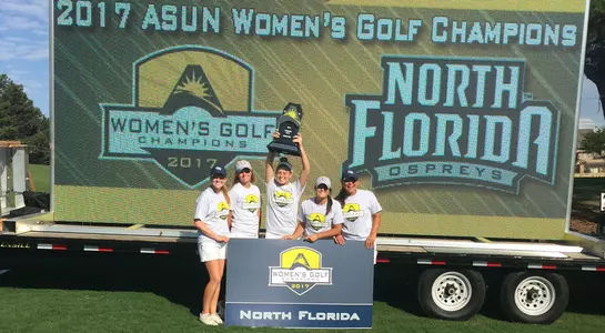 UNF women's golf team poses in front of message board announcing them as ASUN Champions