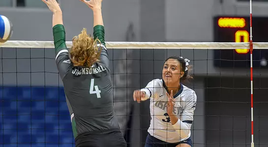 Gabby O'Connell hits a ball past a blocker in a volleyball match.