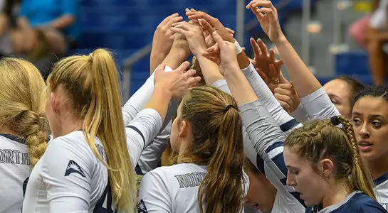 The full team puts their hands together in a huddle during a volleyball match