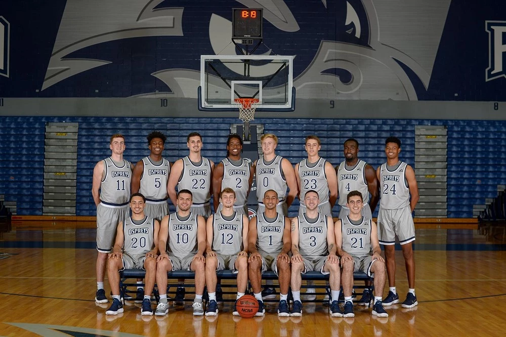 2018-19 North Florida Men's Basketball Team Photo with players in two rows in front of a basketball goal