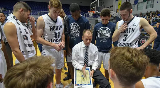 Coach Matthew Driscoll sits in the middle of team huddle during a timeout