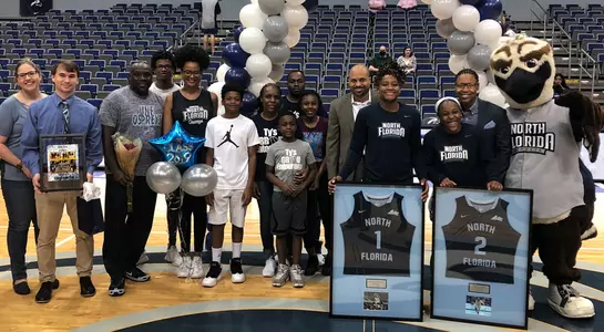 Women's basketball senior class of Ty Purifoy and Arianna Emanuel-Wright along with their families pose together at midcourt