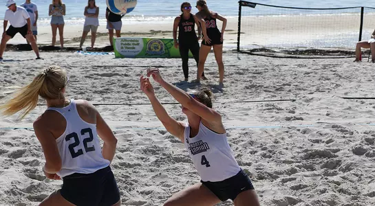 Two Osprey beach volleyball players go for the ball.