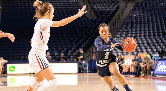 Women's basketball player Ty Purifoy dribbles a basketball with her left hand, attempting to move past a Liberty defender.